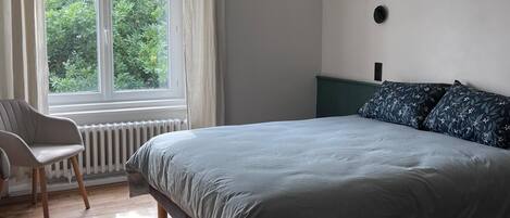 A bedroom with a bed, a chair, a window, and a ceiling fan.