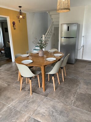 A dining area with a wooden table, six chairs, a vase with flowers, and a stainless steel refrigerator. - Presbytère de Saint Philibert - Beaches on foot (Trégunc)