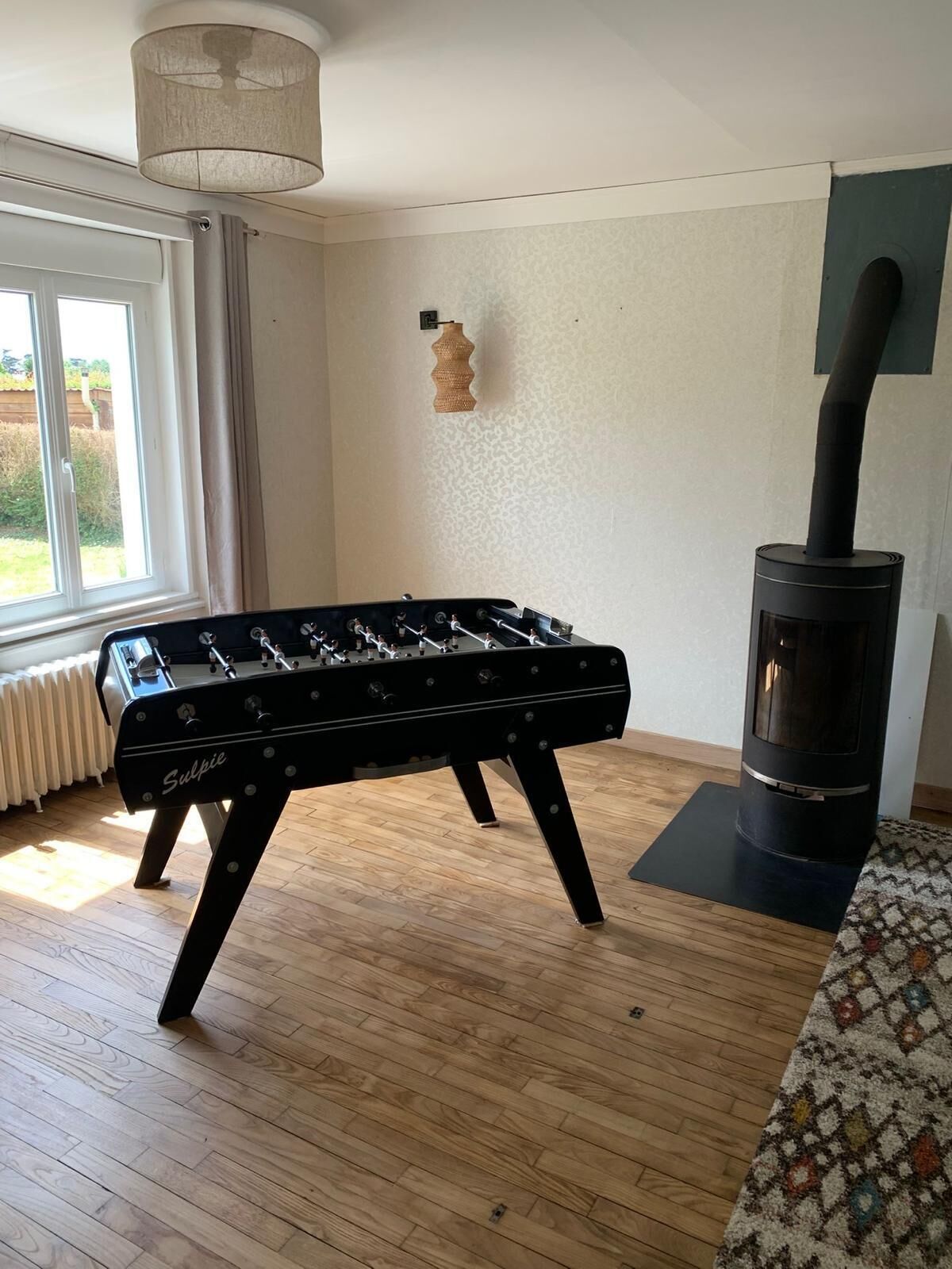 Een kamer met een tafelvoetbaltafel, een houtkachel en een raam met gordijnen.