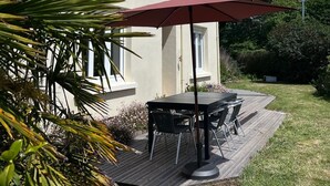 Talo, jossa on patio, pöytä tuoleineen ja punainen aurinkovarjo.