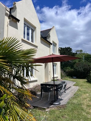 Een huis met een terras, een tafel met stoelen en een rode parasol.