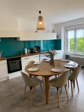 Een moderne keuken met een eethoek, een koffieapparaat en uitzicht op groen.