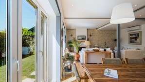A modern kitchen with a stone wall, a dining area with a wooden table, and a large window. - Elegant Garden Villa Cascais by Portugal Portfolio (Cascais)