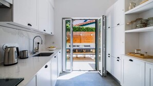A modern kitchen with white cabinetry, a stainless steel kettle, and a glass door leading to an outdoor dining area. - Elegant Garden Villa Cascais by Portugal Portfolio (Cascais)