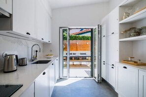 A modern kitchen with white cabinetry, a stainless steel kettle, and a glass door leading to an outdoor dining area.