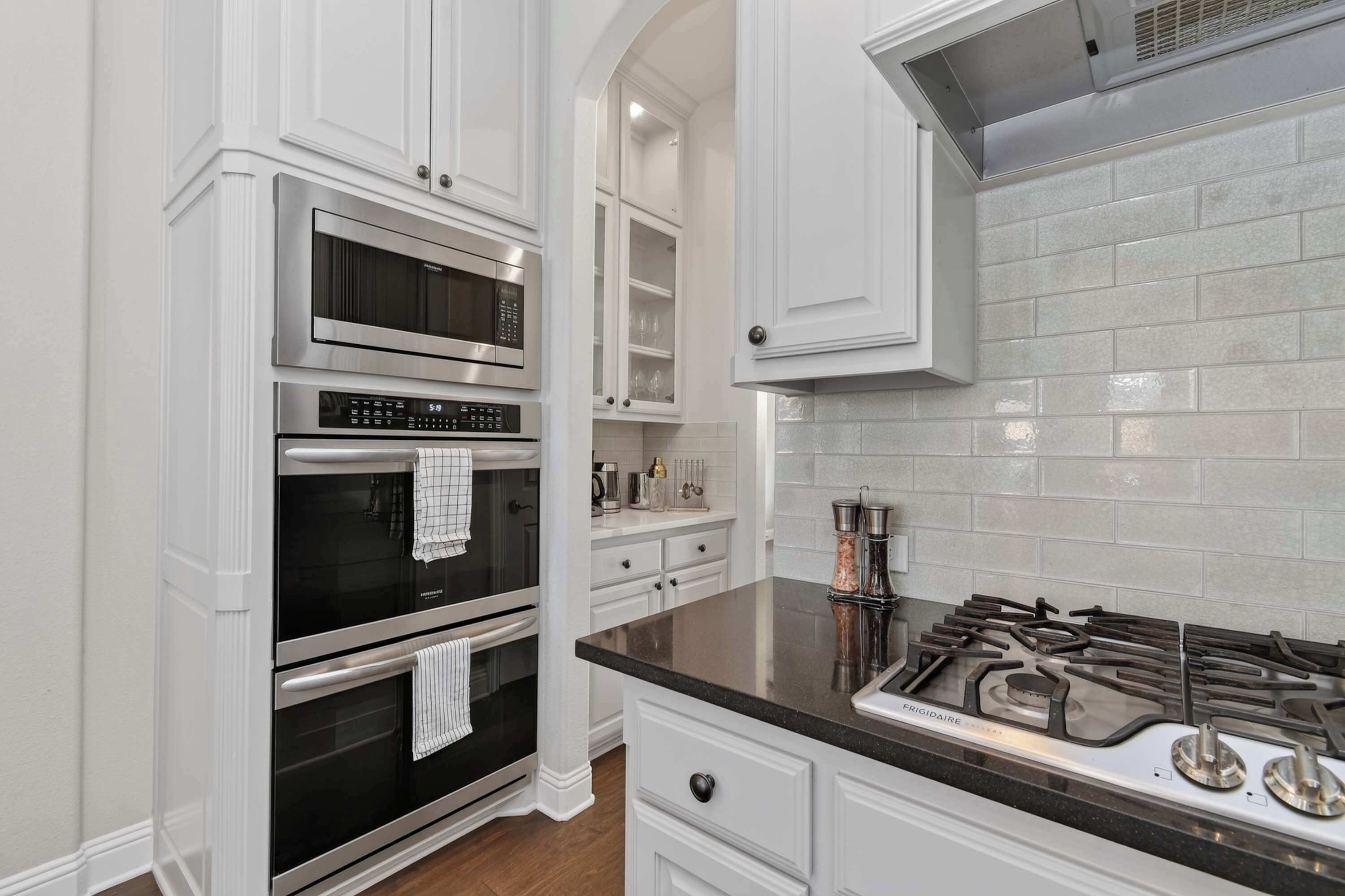 A kitchen with white cabinetry, stainless steel appliances, a black countertop, and a tiled backsplash.