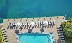 An aerial view of a pool area with sun loungers and umbrellas, surrounded by a clear blue pool and a beach. - Hallandale Beach · 2BR · Intracoastal View (Hallandale Beach)