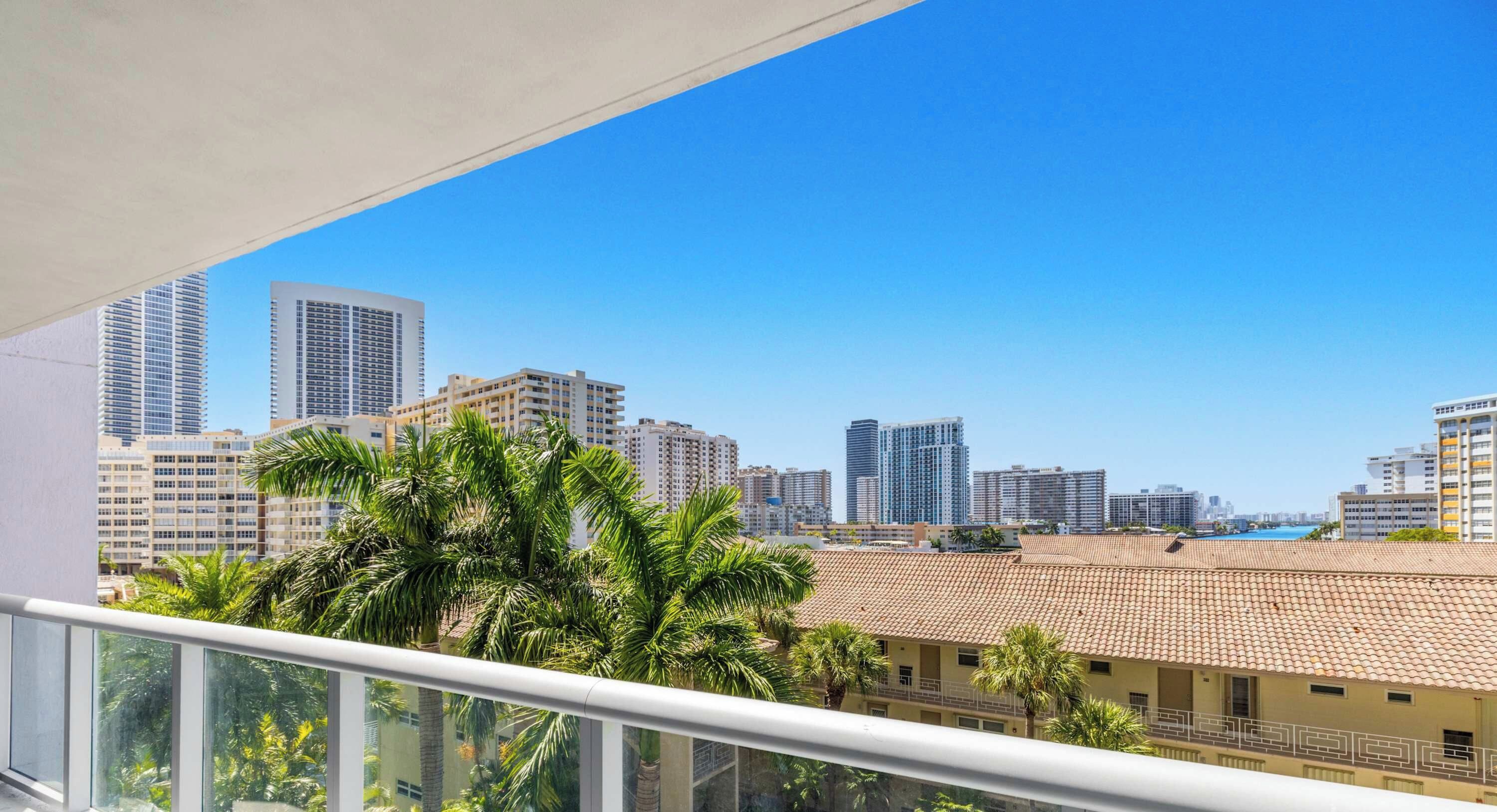 A balcony with a view of a cityscape, including high-rise buildings and palm trees.