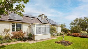 Une maison dotée de panneaux solaires, d’une véranda et d’un jardin bien entretenu.