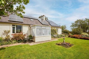 Een huis met zonnepanelen, een tuinkamer en een verzorgde tuin.