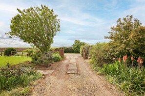 A gravel path leading to a wooden gate, surrounded by greenery and a clear sky.