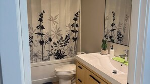 Un baño con inodoro, lavabo con espejo y cortina de ducha con motivos florales.