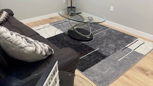Una sala de estar con una mesa de centro de vidrio, un sofá, un televisor, un adorno de pared y una planta.