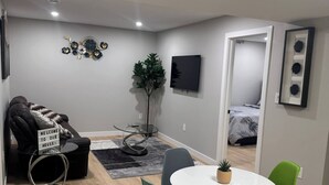 Una sala de estar moderna con un sofá, una mesa de centro, una mesa de comedor con sillas, un televisor y una planta.