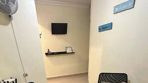 A room with two black chairs with green cushions, a white table with decorative items, a wall-mounted fan, and a shelf with a framed picture and small items. - Cozy, Centric Apartment in Central Santo Domingo Este (Santo Domingo Este)