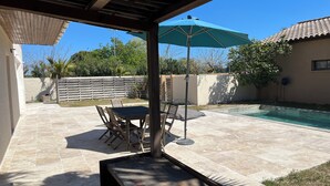 Un patio con piscina, mobiliario de madera y una zona cubierta.