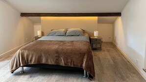 Un dormitorio con cama, vigas de madera, una mesita de noche y una lámpara.