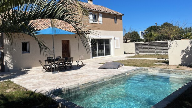 Una casa de dos pisos con piscina, muebles de exterior y una palmera.