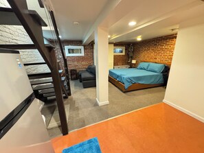 Ein Schlafzimmer mit Bett, einer kleinen Sitzecke, einem Fernseher und einer Ziegelwand.