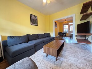 Ein Wohnzimmer mit einem Ecksofa, einem Couchtisch aus Holz und einer TV-Konsole.