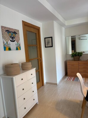 Ein Zimmer mit einem weißen Kommode, einer Holztür, einem gerahmten Kunstwerk, einem Spiegel und einer Topfpflanze.