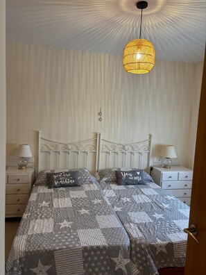 Ein Doppelbett mit einem sternenmusterbedeckten Überwurf, zwei Nachttische mit Lampen, eine Hängelampe und ein an der Wand befestigter Schlüsselhalter.