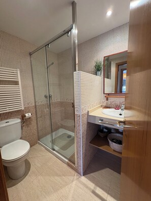 Ein Badezimmer mit Duschkabine aus Glas, Toilette, Waschbecken mit Spiegel und einer gefliesten Rückwand.