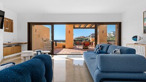 Un salon moderne avec un canapé, une table basse et un téléviseur. Une porte-fenêtre coulissante donne accès à un patio extérieur équipé d’une table et de chaises.