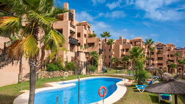 Une piscine entourée de palmiers et un bâtiment doté de balcons.