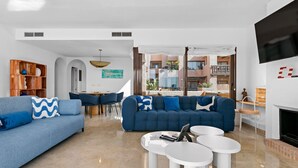 Un salon moderne avec un canapé bleu, des tables basses blanches et un téléviseur fixé au mur.