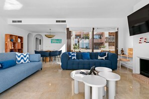 A modern living room with a blue sofa, white coffee tables, and a TV mounted on the wall. - Coto Real Penthouse 2470 Naxos Sea View (Manilva)