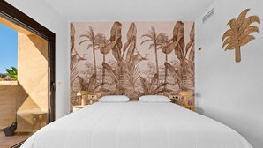 Une chambre avec un lit, deux tables de chevet, une fresque murale représentant une végétation tropicale et une porte donnant sur un espace extérieur.