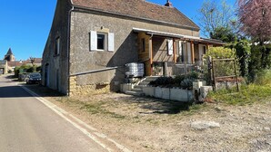 A stone house with a tiled roof, a porch, and a fenced garden area.