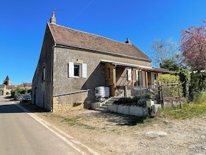 Une maison en pierre avec un toit en tuiles, un porche et un jardin clos.