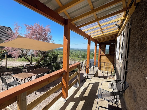 Une terrasse extérieure couverte, aménagée avec des meubles en bois et offrant une vue sur la campagne.