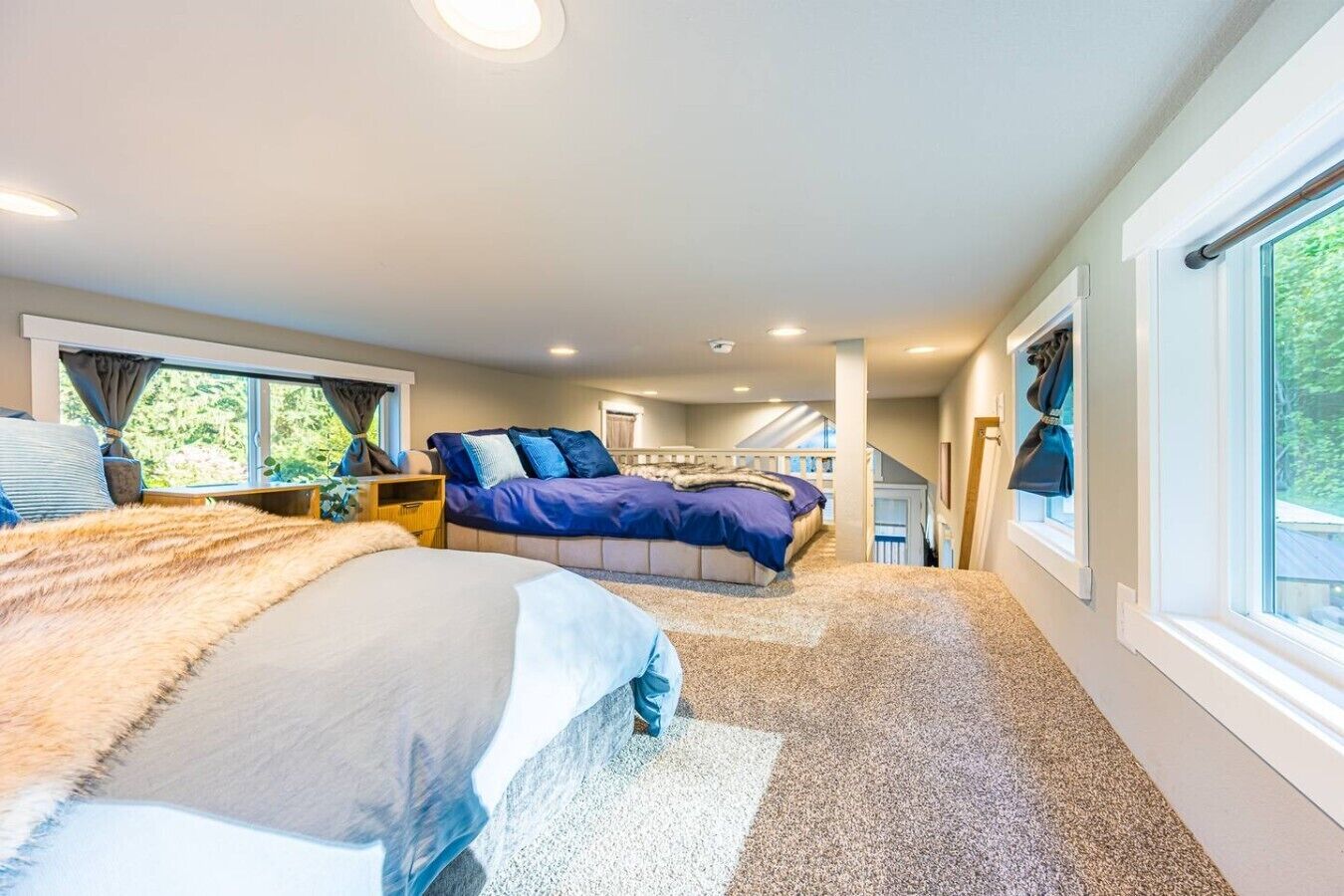 A bedroom with a large bed, a smaller bed, a window, and a staircase leading to an upper level.