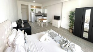 A modern hotel room with a bed, a sofa, a dining table, and a TV. - LOS CORALES del Mar STUDIOS & SUITES SPA (Punta Cana)