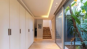 A hallway with a wooden floor, white walls, and a staircase leading to a room.