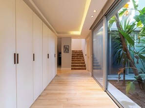A hallway with a wooden floor, white walls, and a staircase leading to a room.