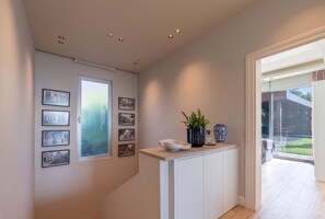 Un couloir avec un escalier, une porte donnant sur un balcon et un mur orné de tableaux encadrés.