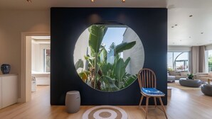 A modern living room with a circular window, a wooden floor, a round rug, and a chair with a blue cushion.