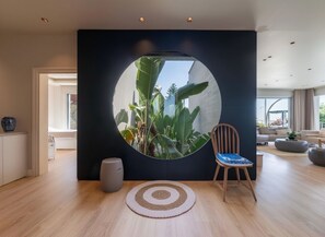 A modern living room with a circular window, a wooden floor, a round rug, and a chair with a blue cushion.
