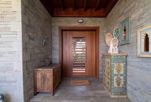 A wooden door with a slatted design, a bench, a decorative cabinet, and a doormat with the word 'yuva.'
