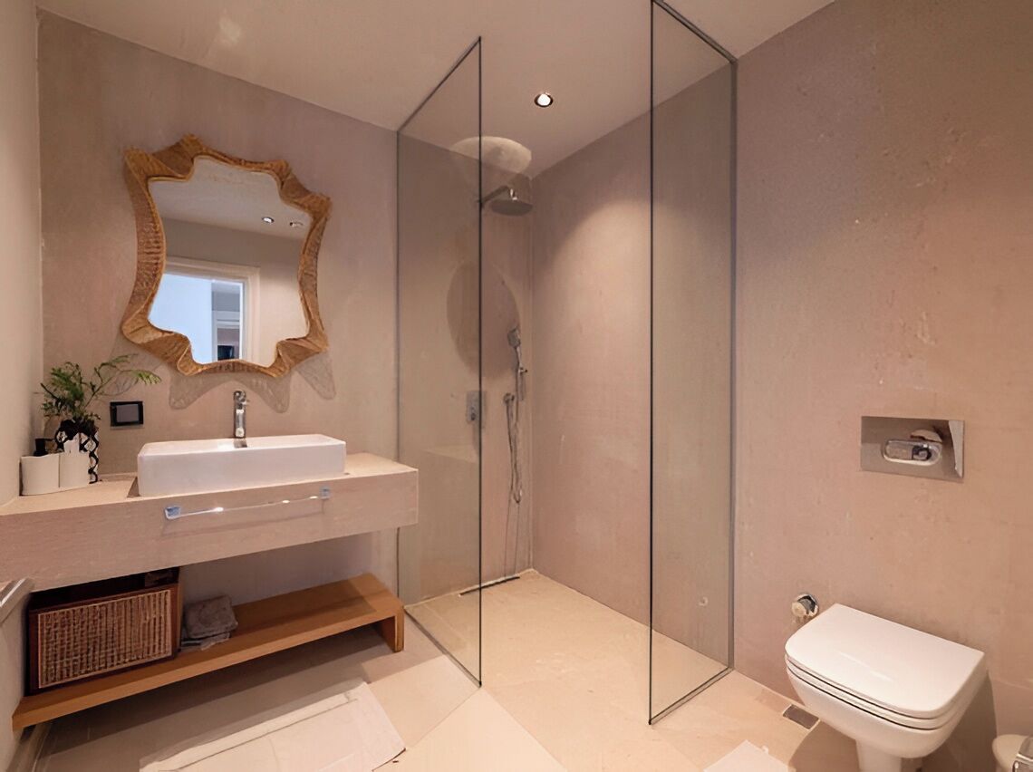 Un baño moderno con cabina de ducha de vidrio, un lavabo blanco con espejo y un inodoro.