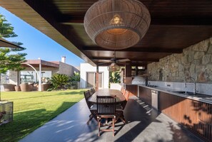 An outdoor dining area with a round table and chairs, a hanging light fixture, and a stone wall.