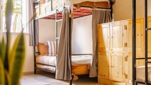 A room with a bunk bed, a wooden cabinet, and a hanging light fixture. - Sable Beach Surfcamp Tamraght  (Aourir)
