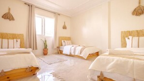 A hotel room with three beds, a large window, and a potted plant. - Sable Beach Surfcamp Tamraght  (Aourir)