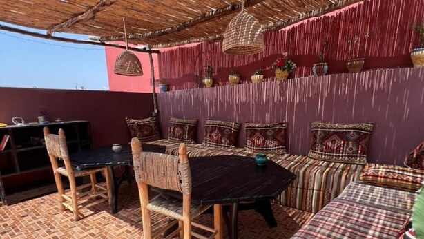 An outdoor seating area with a table and chairs, a sofa, and a patterned wall. - Sable Beach Surfcamp Tamraght  (Aourir)