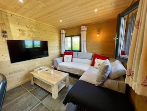 Ein gemütliches Interieur einer Holzhütte mit einer Couch, einem Fernseher und einem Holztisch.