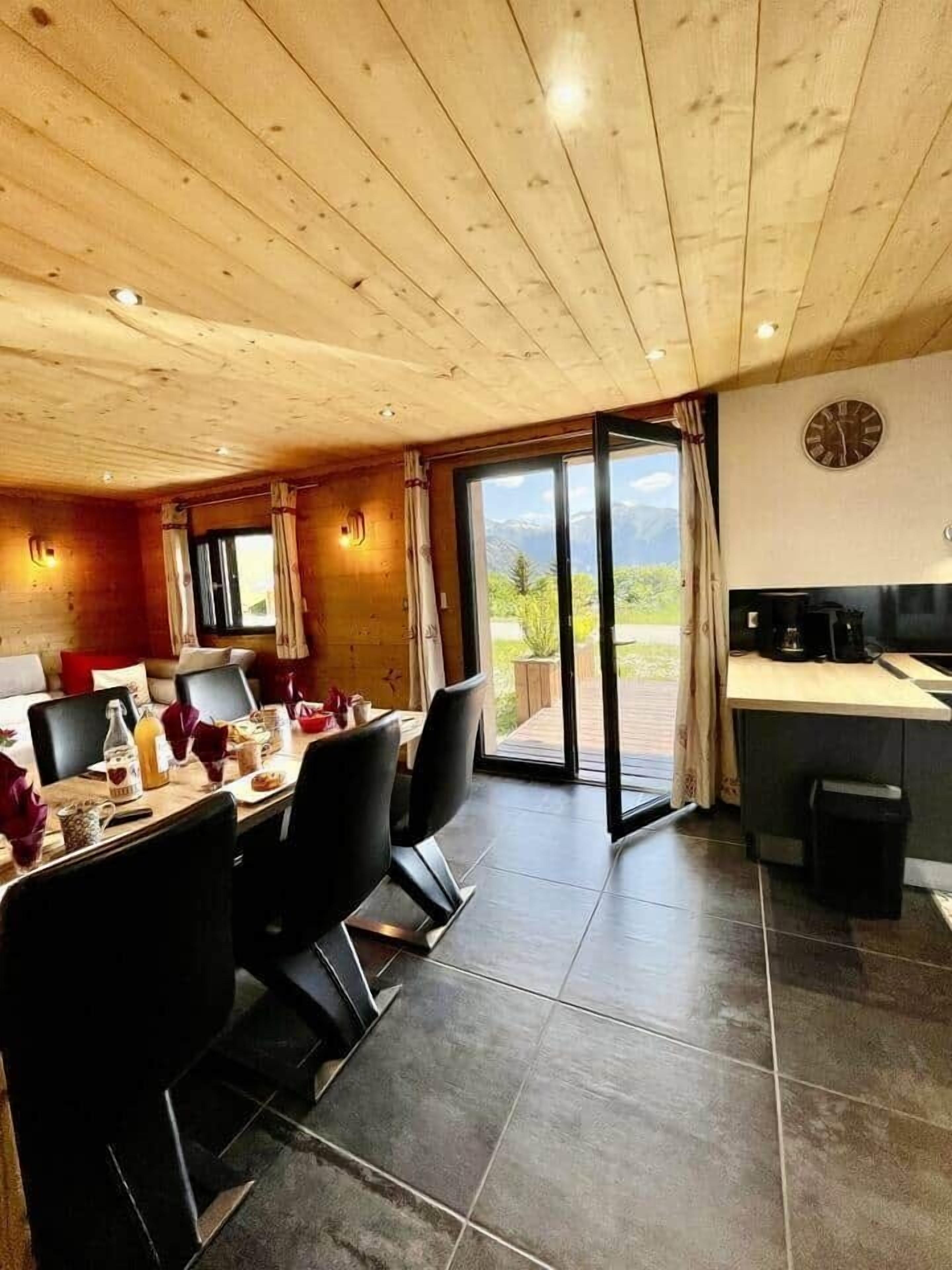 A dining area with a table set for four, a kitchen area with a sink and stove, and a sliding glass door leading to a balcony with a mountain view.